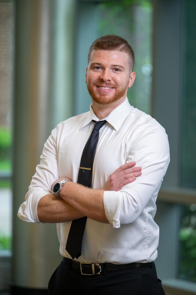 Headshot of John Saxton is a white button-up and tie, posing with his arms crossed.