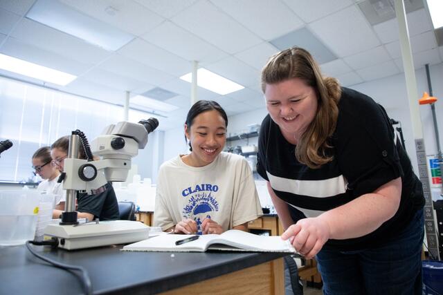 A McDaniel research student and professor look at a notebook next to a microscope.