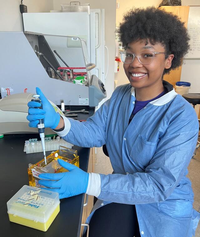 A student in a blue lab coat holds a syringe.