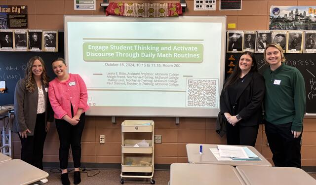 Three McDaniel faculty members pose behind a table with a McDaniel banner.