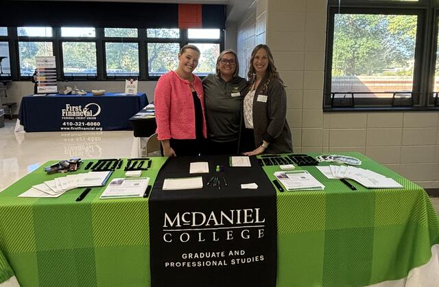 A McDaniel student and two faculty members pose behind a table with a McDaniel banner.