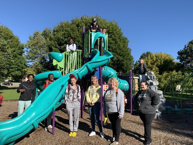 A group of students standing around a green big slide at a children's park