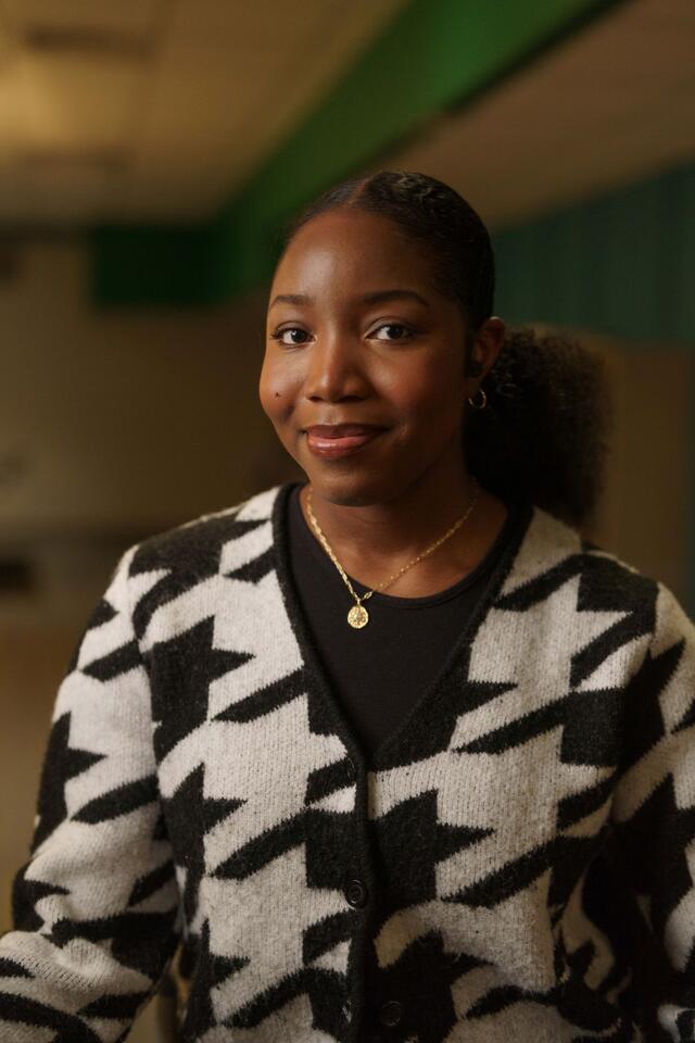 Portrait of Olivia "Kaami" Effa indoors. She is wearing a black and white patterned cardigan.