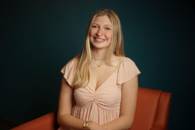 Headshot of Madge Myers on an orange couch while wearing a pink blouse.