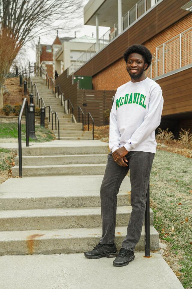 Olanrewaju Abayomi stands outside in front of a staircase wearing a McDaniel sweatshirt.