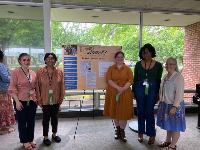 A group of students poses next to a poster about the Westminster Detective Library.