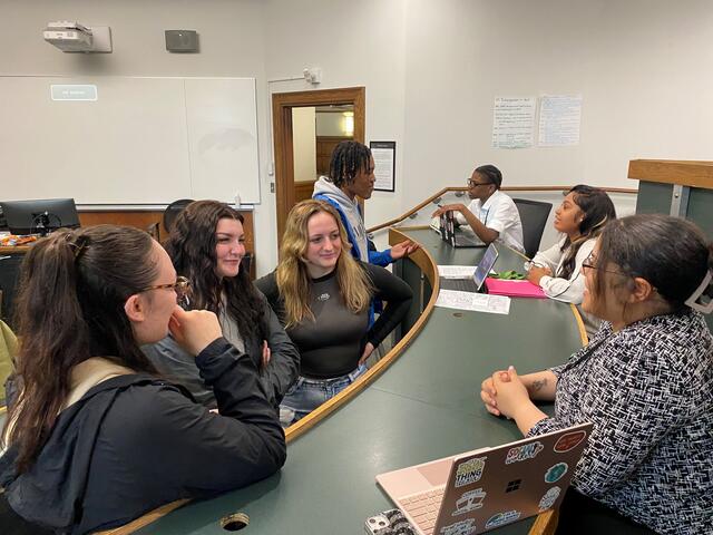 A student with a laptop next to her speaks to group.