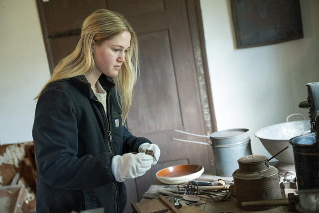 Student Alicia Heard wears white gloves to handle historical cooking tools.