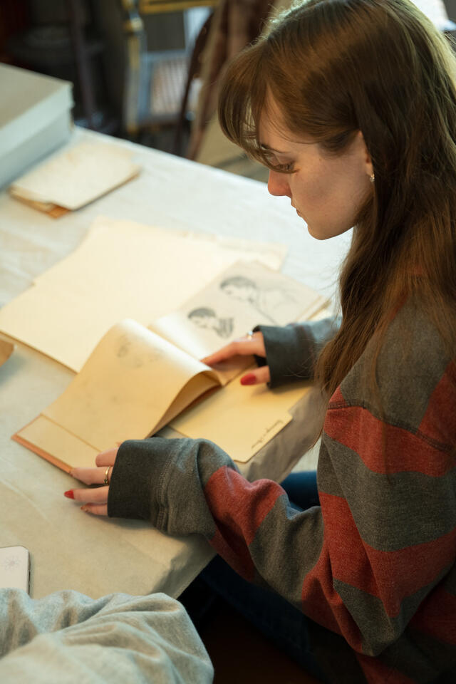 A student sits at a table and looks at an old notebook.