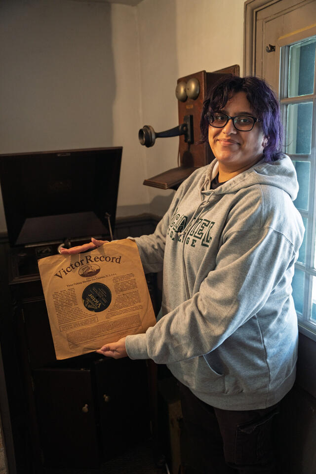 Sherlyn Estrada Holds up a record in front of a Victrola.