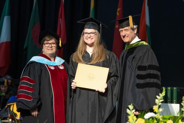 Hodge Award recipient on stage with Dean of Graduate and Professional Studies Vickie Mazer and Chair of the Board of Trustees Bruce Preston at Commencement.