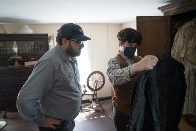 A student stands with the director of Union Mills Homestead while holding up historical clothing.