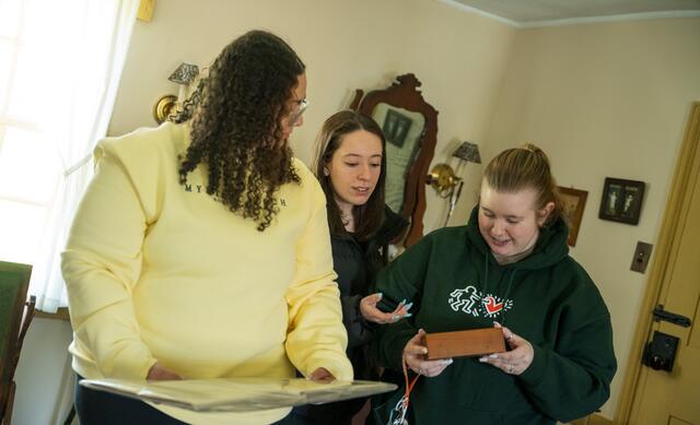 Three students look down at an old-fashioned children's toy.