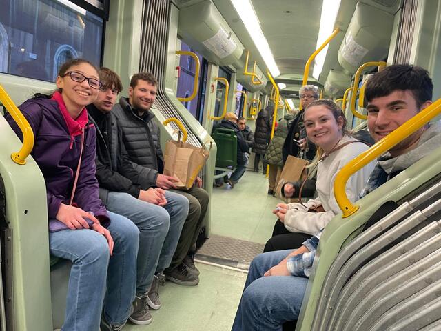 A group of students seated on a bus smile at the camera.