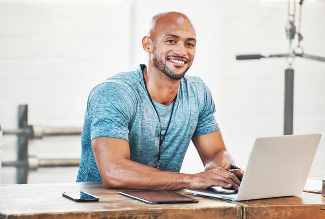 A man types on a laptop in a gym.
