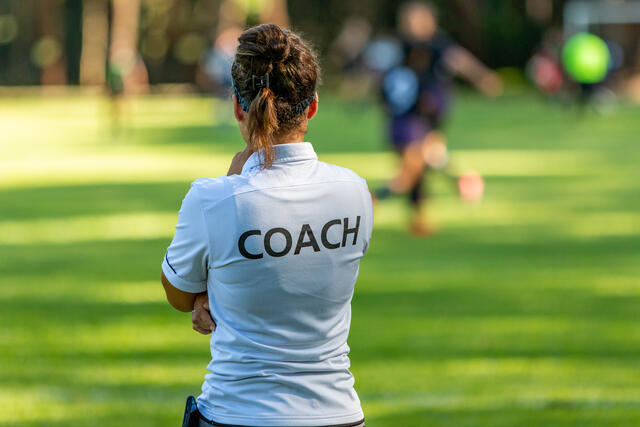A woman wearing a "Coach" shirt watches a soccer match.