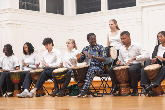 African Drum Ensemble sits on stage in front of drums