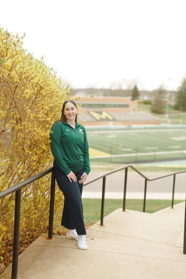 A female student in McDaniel athletic gear stands on the stairs leading down to the football field.