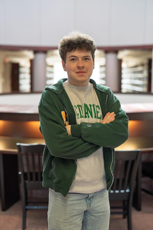 A male student stands with his arms crossed in Hoover Library.