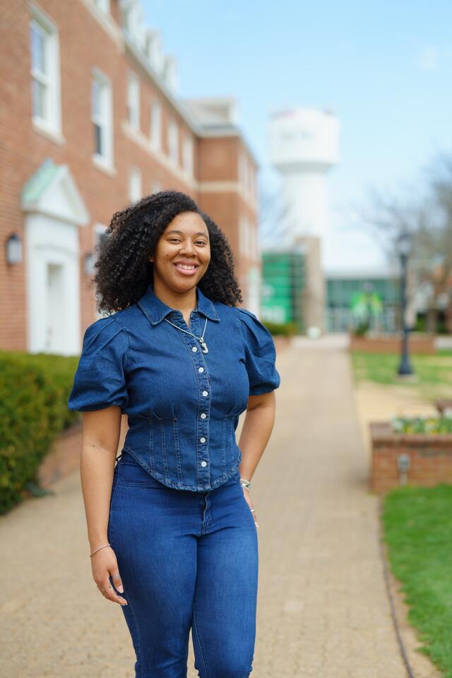 A female student in a denim outfit stands with her hand on her hip outside a McDaniel dorm building.