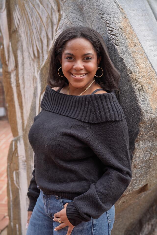 A female student in a black sweater poses in front of a rock statue.