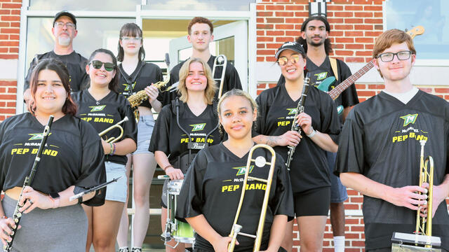Band director with 9 students wearing black jerseys with the McDaniel Athletic Logo and the words Pep Band and holding various instruments