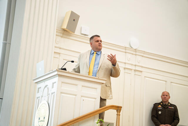 A man in a light-colored suit speaks at a podium.