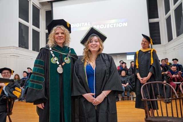 President Jasken and Delaney O'Conner, both in graduation regalia, stand on the stage