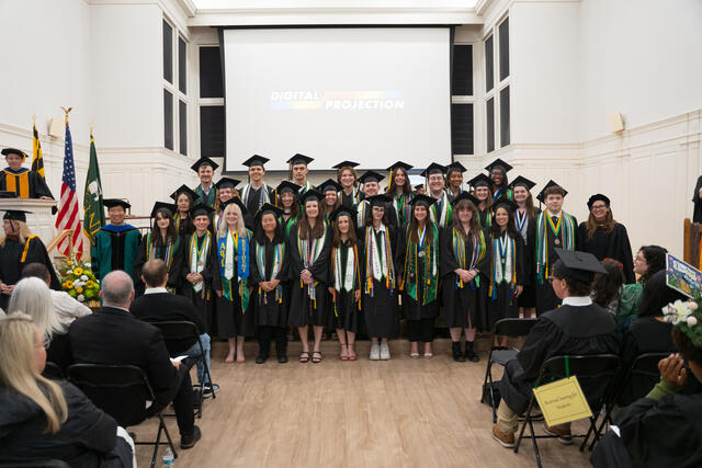 Group of students in graduation regalia pose on stage