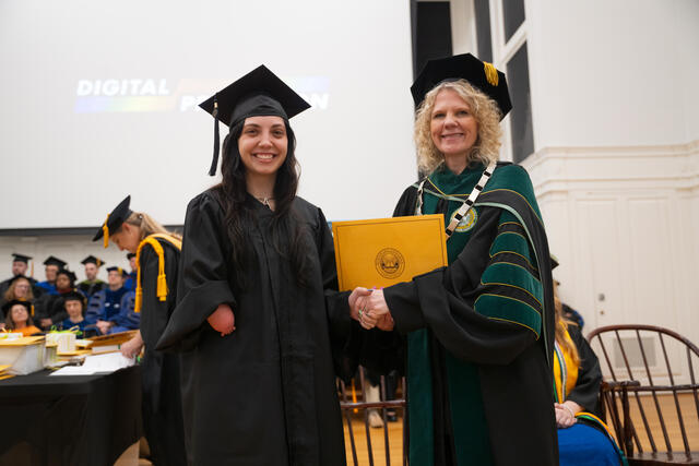 Student in graduation regalia poses with President Julia Jasken, also in graduation regalia
