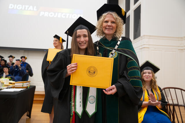 Student in graduation regalia poses with President Julia Jasken, also in graduation regalia