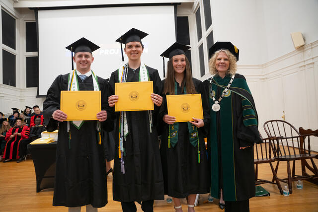 Students in graduation regalia pose with President Julia Jasken, also in graduation regalia
