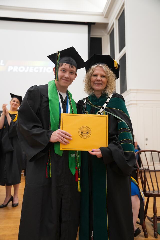 Student in graduation regalia poses with President Julia Jasken, also in graduation regalia