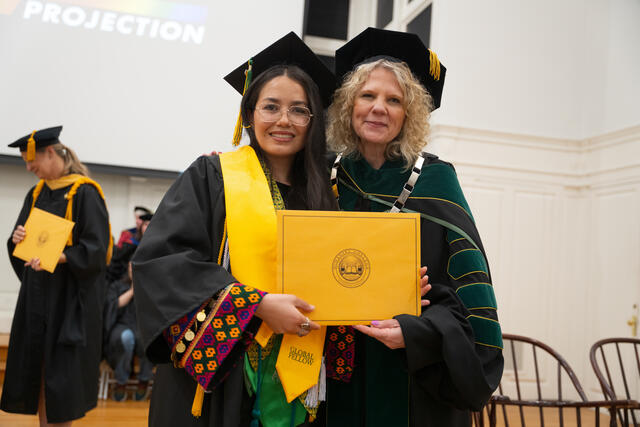 Student in graduation regalia poses with President Julia Jasken, also in graduation regalia