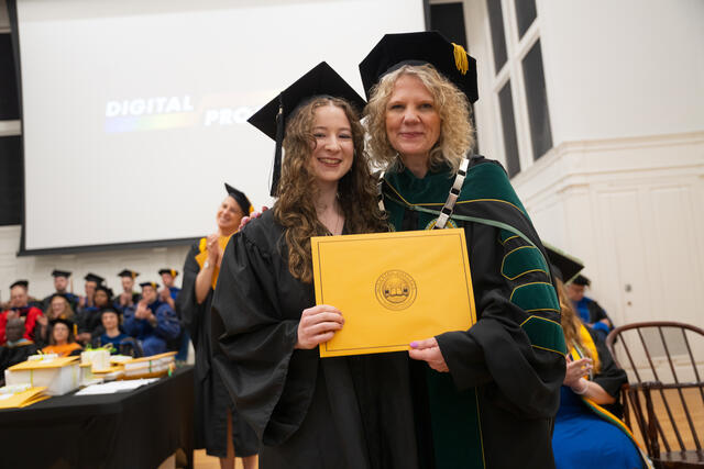 Student in graduation regalia poses with President Julia Jasken, also in graduation regalia