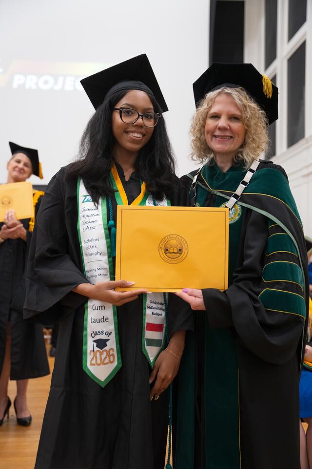 Student in graduation regalia poses with President Julia Jasken, also in graduation regalia