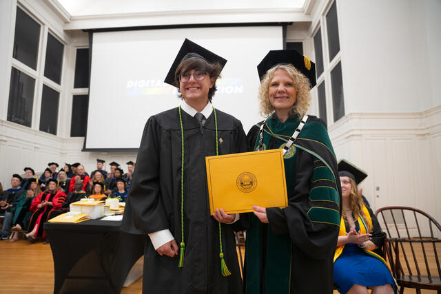 Student in graduation regalia poses with President Julia Jasken, also in graduation regalia
