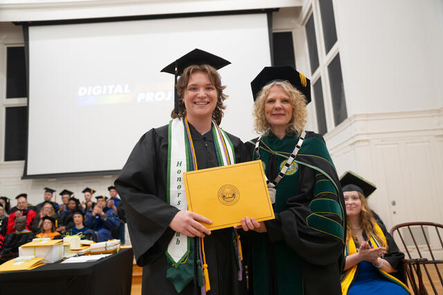 Student in graduation regalia poses with President Julia Jasken, also in graduation regalia
