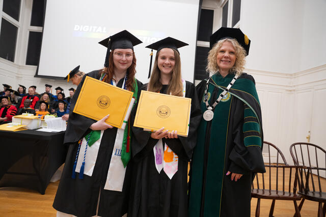 Students in graduation regalia pose with President Julia Jasken, also in graduation regalia