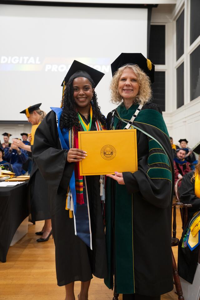 Student in graduation regalia poses with President Julia Jasken, also in graduation regalia