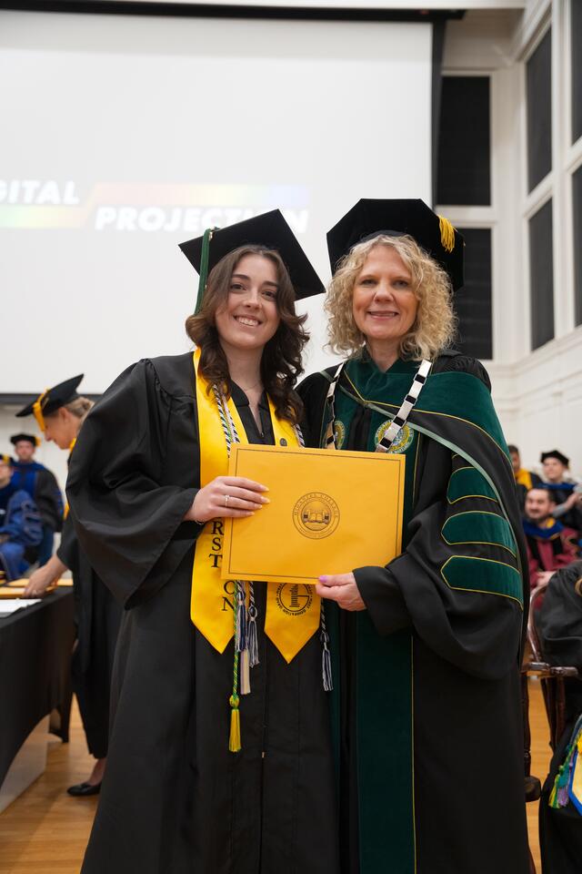 Student in graduation regalia poses with President Julia Jasken, also in graduation regalia