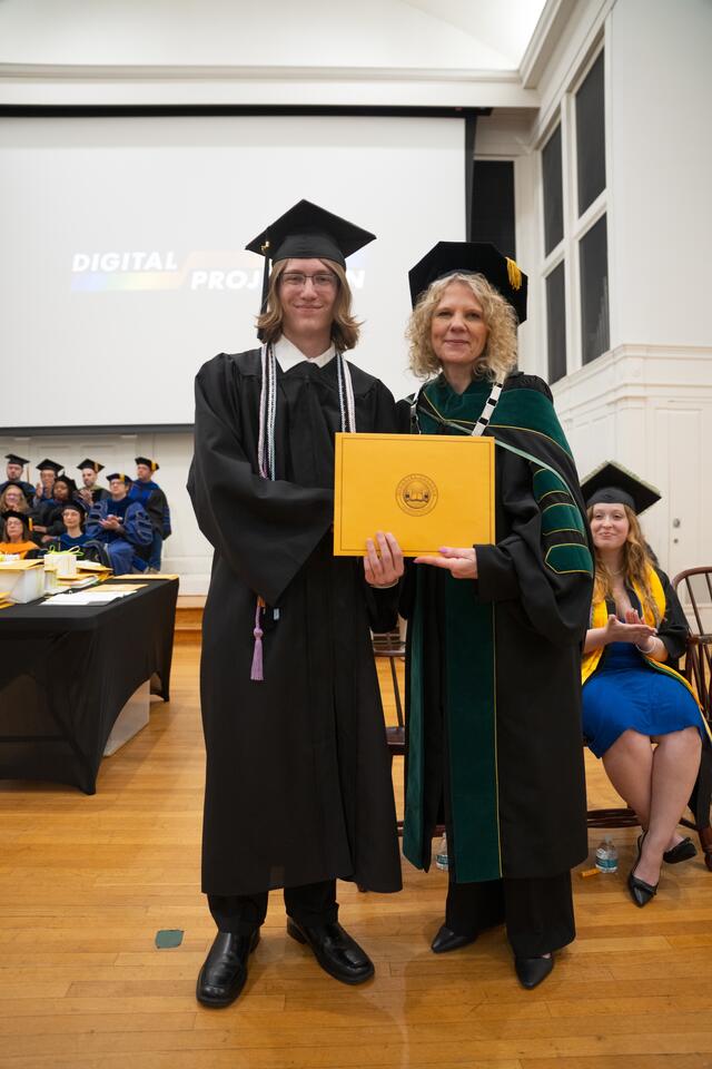 Student in graduation regalia poses with President Julia Jasken, also in graduation regalia