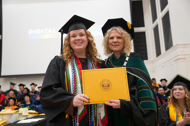 Student in graduation regalia poses with President Julia Jasken, also in graduation regalia