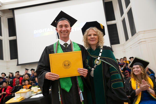 Student in graduation regalia poses with President Julia Jasken, also in graduation regalia