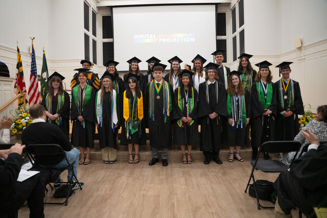 Group of students in graduation regalia pose on stage