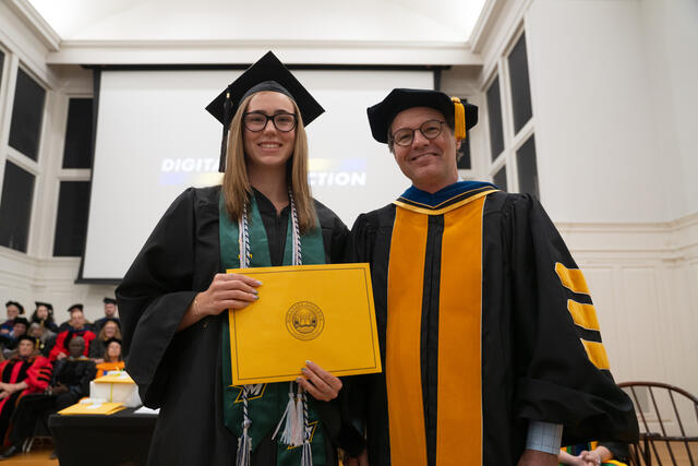 Student in graduation regalia poses with Provost Flavius Lilly, also in graduation regalia