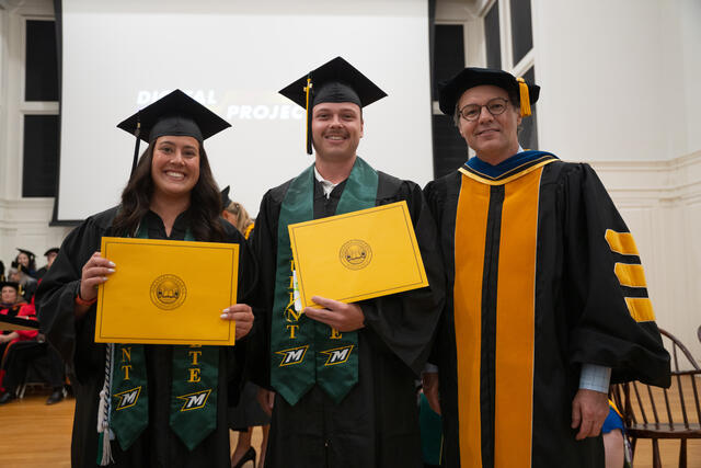 Student in graduation regalia poses with Provost Flavius Lilly, also in graduation regalia