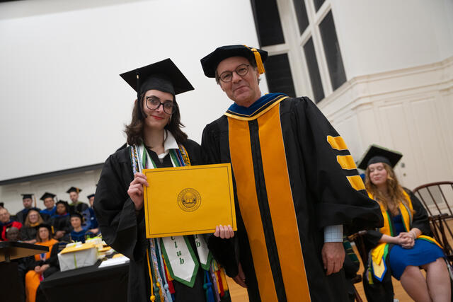 Student in graduation regalia poses with Provost Flavius Lilly, also in graduation regalia