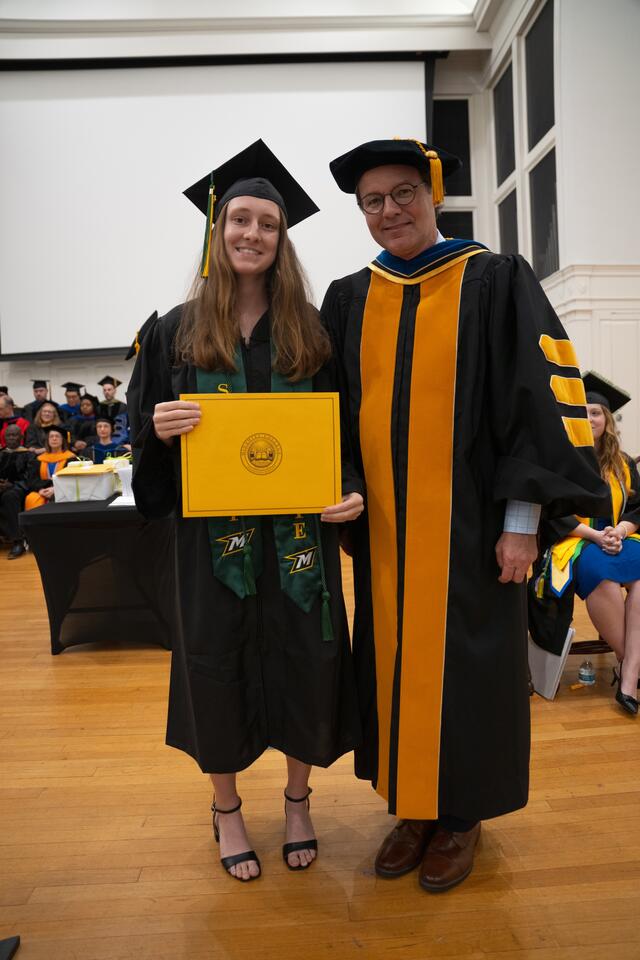 Student in graduation regalia poses with Provost Flavius Lilly, also in graduation regalia