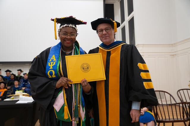 Student in graduation regalia poses with Provost Flavius Lilly, also in graduation regalia